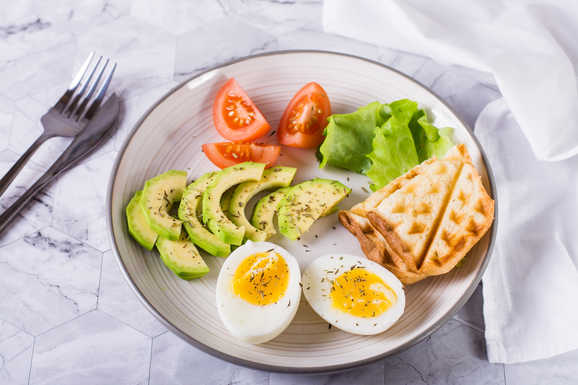 Avocado, soft boiled egg, tomatoes, lettuce and toast on a plate. Healthy food.